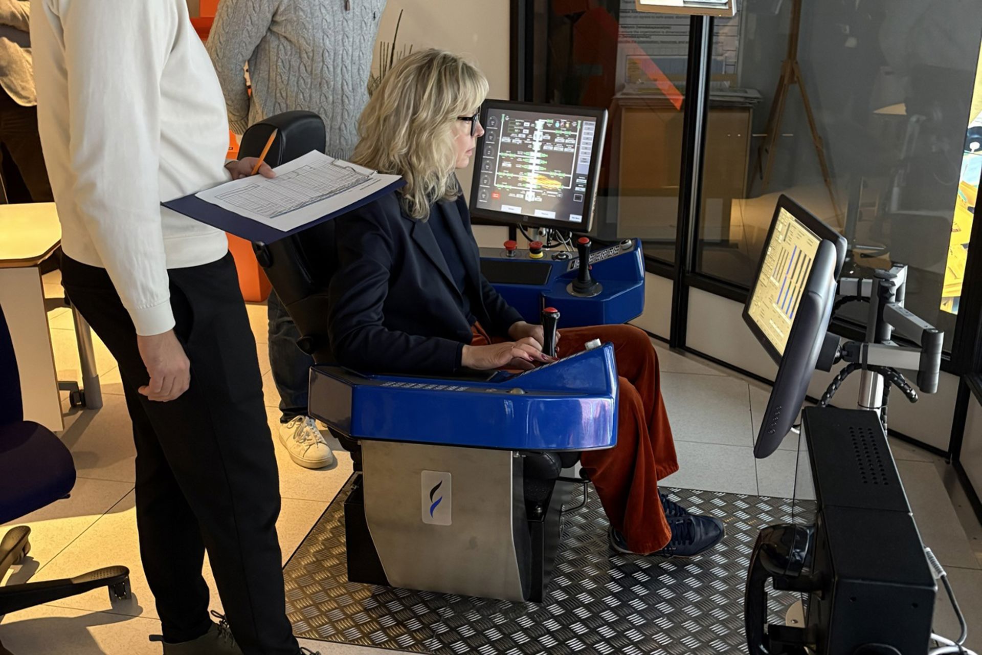 Bildet viser statsråden som sit i ein simulator, med to studentar på sida av ho.