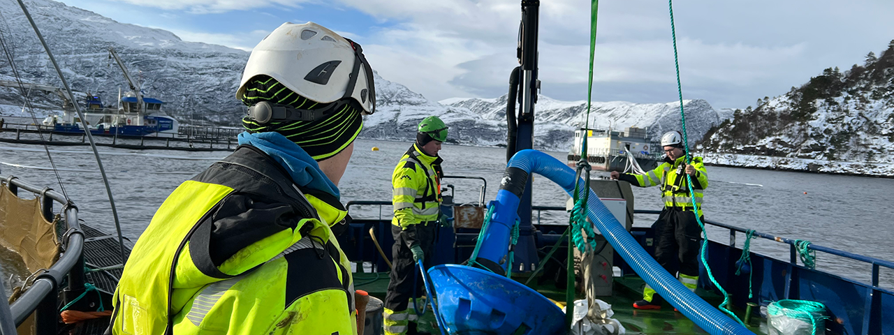 Tre personar som arbeider ombord i ein servicebåt ved eit oppdrettsanlegg.